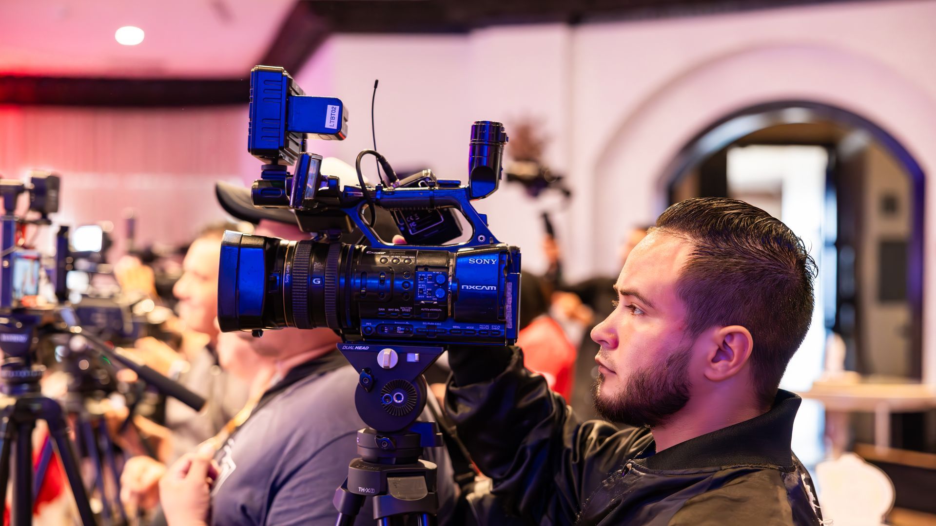 Camarógrafo grabando con cámara de video en trípode durante un evento